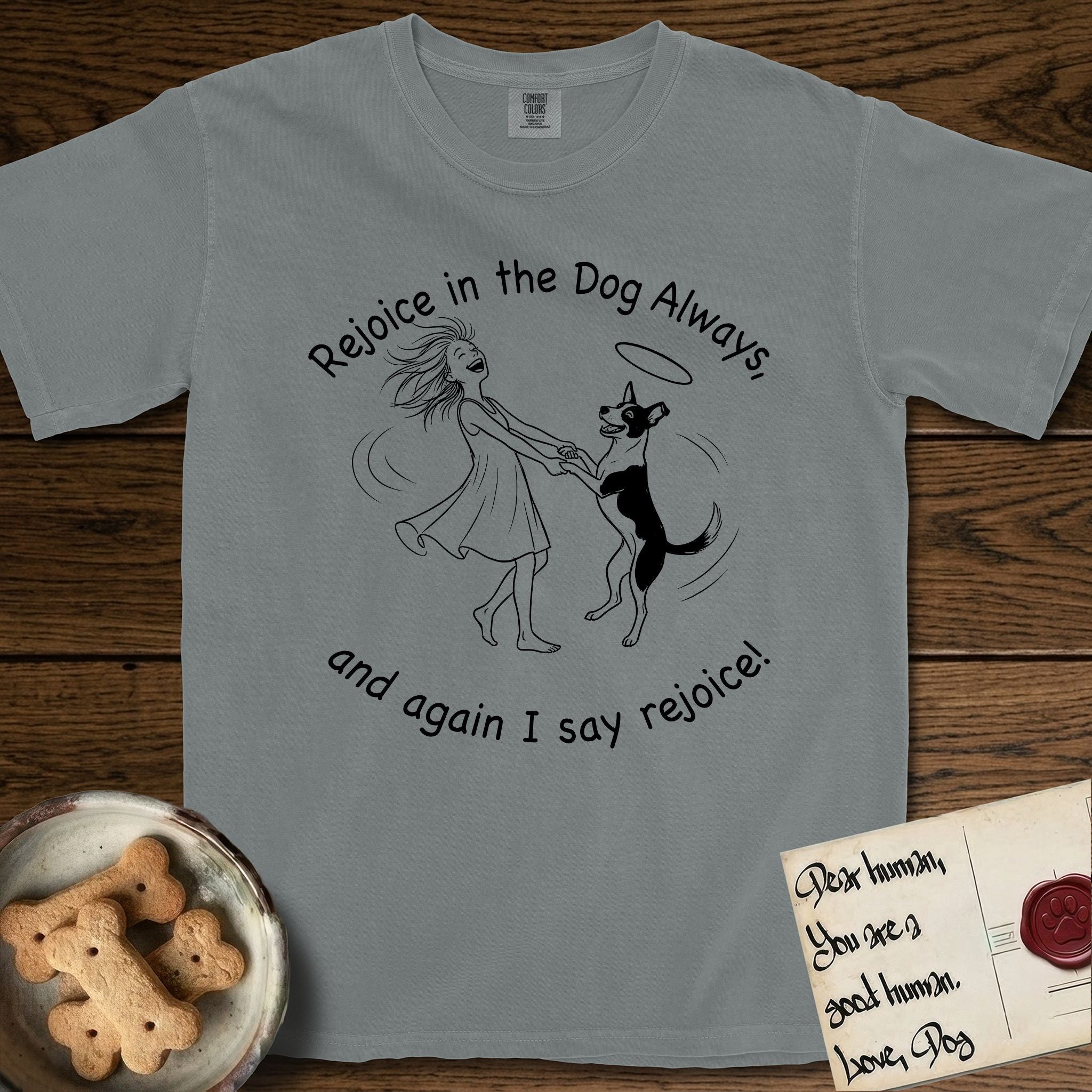 Rejoice in the Dog Lobo T-Shirt flat lay in Granite, featuring a sparse pen-and-ink illustration of a girl and her haloed Dog Lobo spinning together, hands and paws clasped.