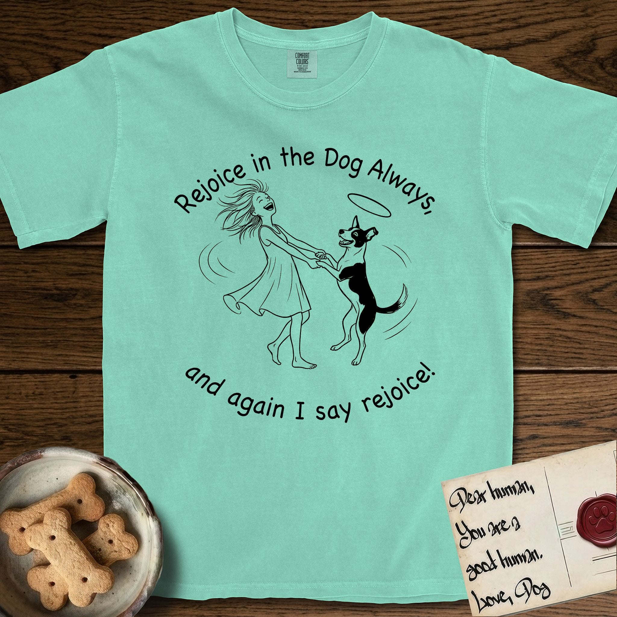 Rejoice in the Dog Lobo T-Shirt flat lay in Island Reef, featuring a sparse pen-and-ink illustration of a girl and her haloed Dog Lobo spinning together, hands and paws clasped.