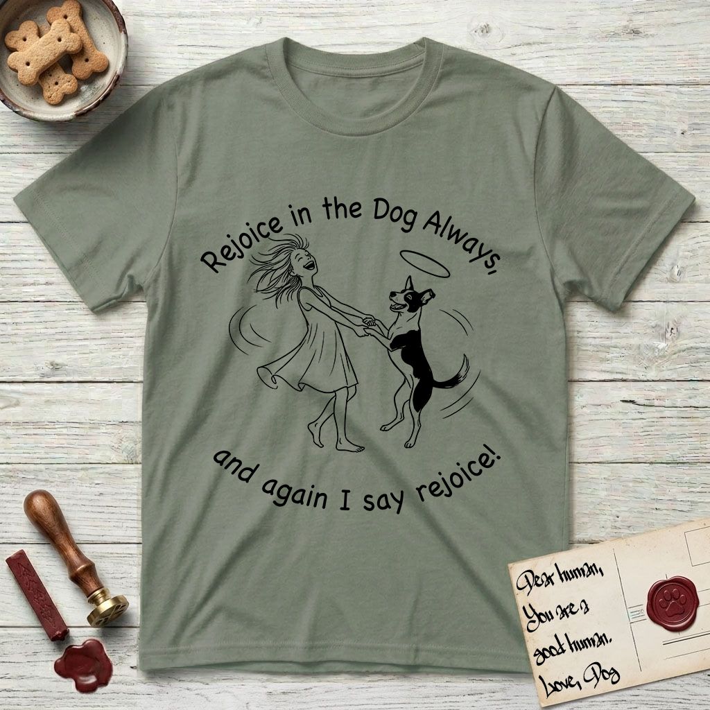 Rejoice in the Dog Lobo T-Shirt flat lay in Sage, featuring a sparse pen-and-ink illustration of a girl and her haloed Dog Lobo spinning together, hands and paws clasped.