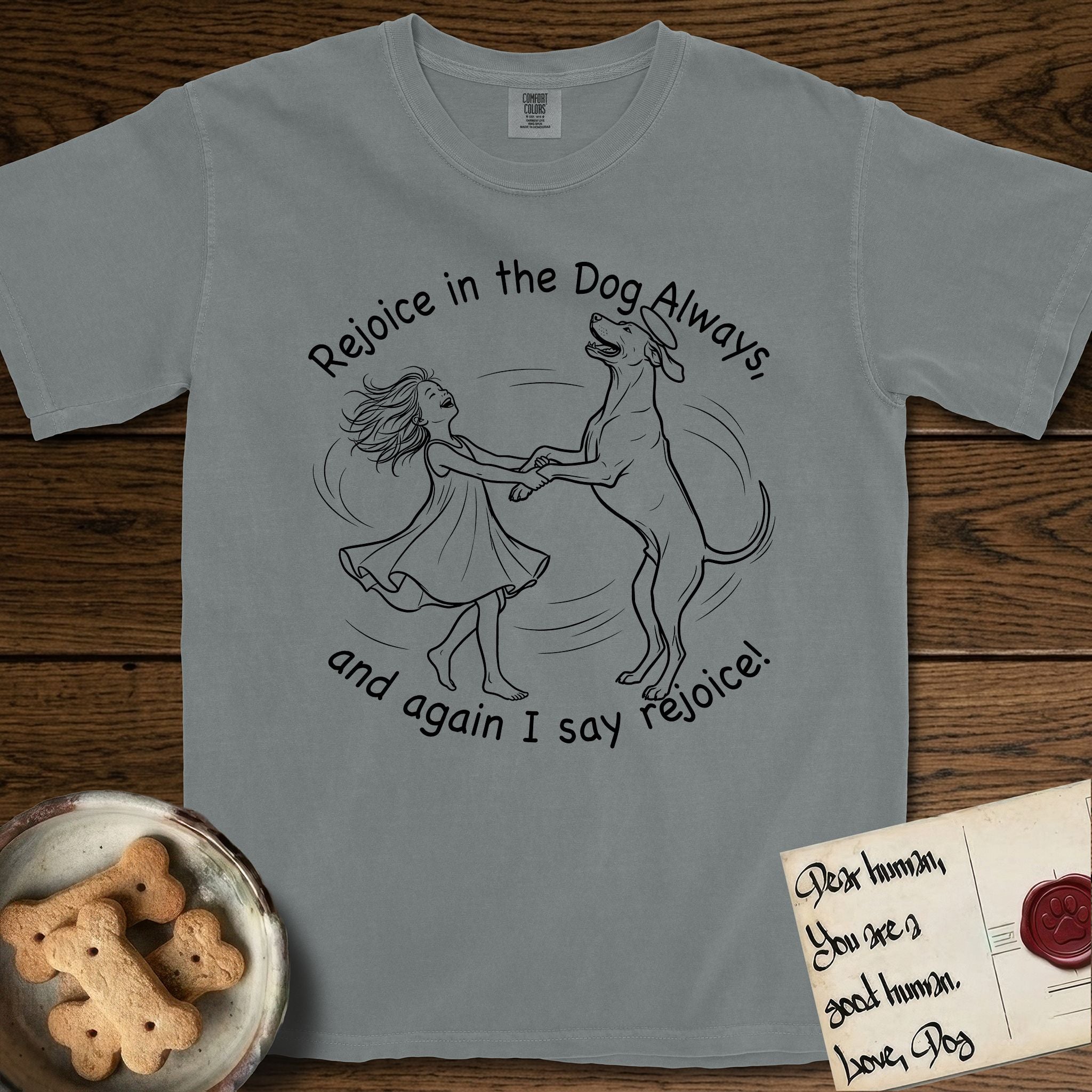Rejoice in the Dog Rhodesian Ridgeback T-Shirt flat lay in Granite, featuring a sparse pen-and-ink illustration of a girl and her Rhodesian Ridgeback spinning together, hands and paws clasped.