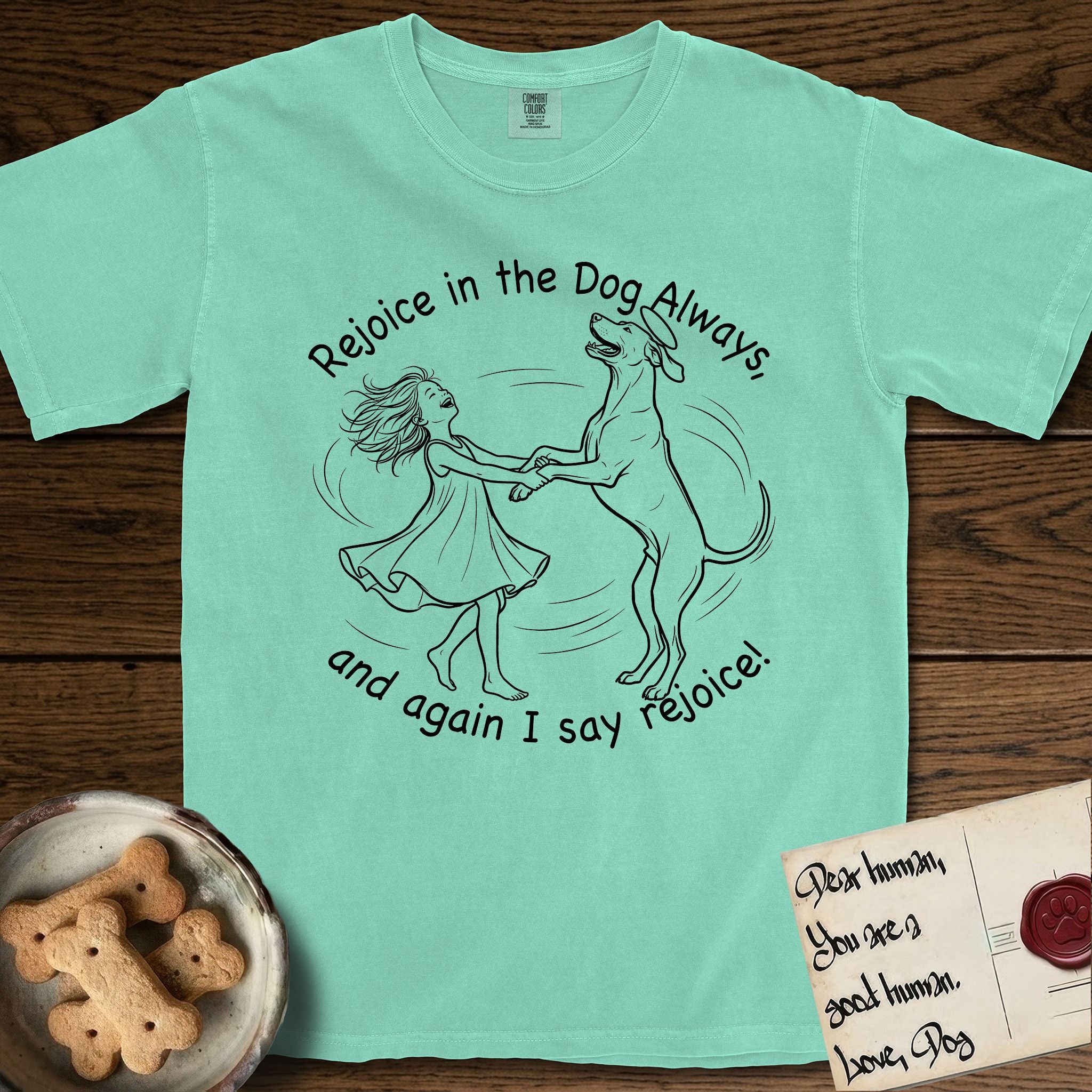 Rejoice in the Dog Rhodesian Ridgeback T-Shirt flat lay in Island Reef, featuring a sparse pen-and-ink illustration of a girl and her Rhodesian Ridgeback spinning together, hands and paws clasped.