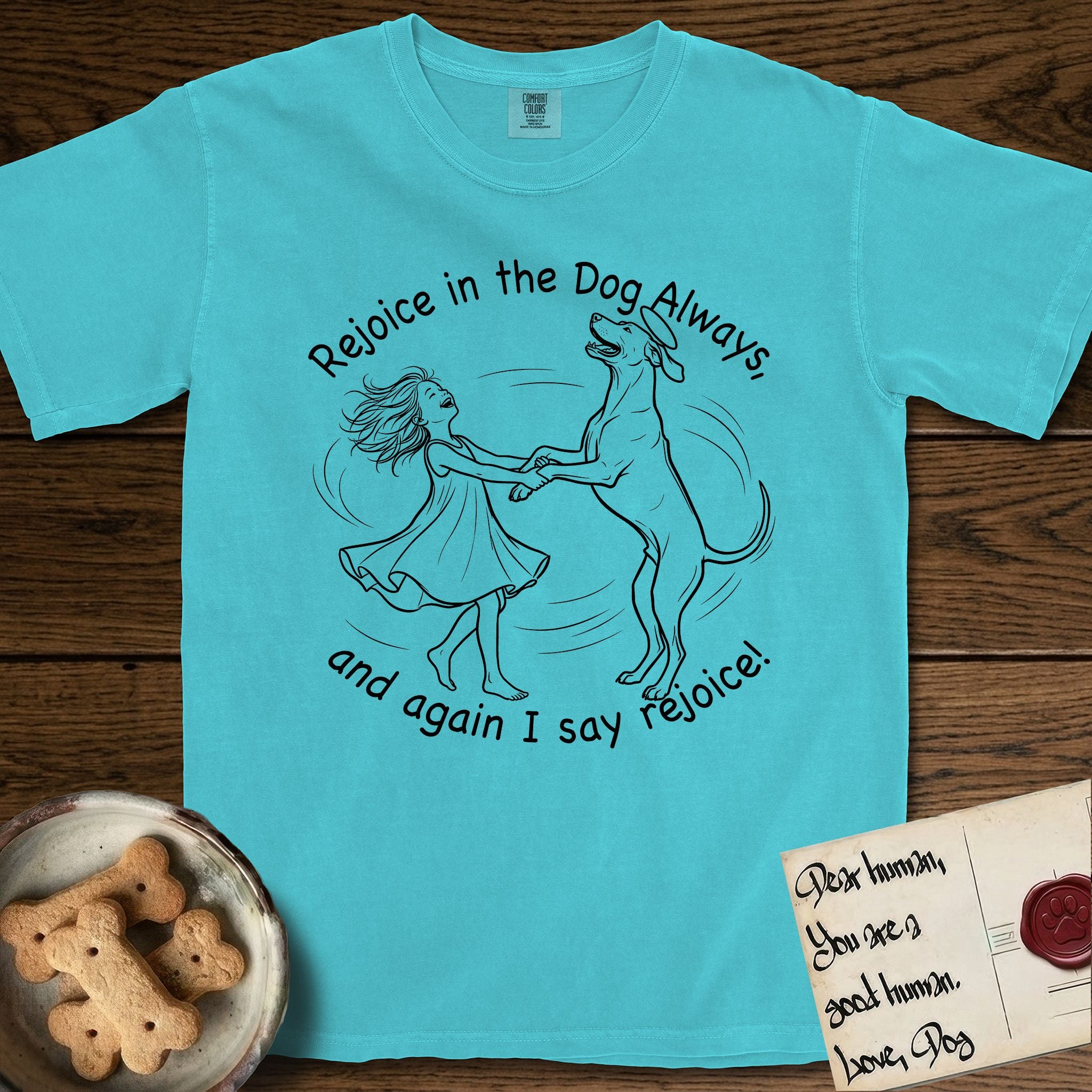 Rejoice in the Dog Rhodesian Ridgeback T-Shirt flat lay in Lagoon Blue, featuring a sparse pen-and-ink illustration of a girl and her Rhodesian Ridgeback spinning together, hands and paws clasped.