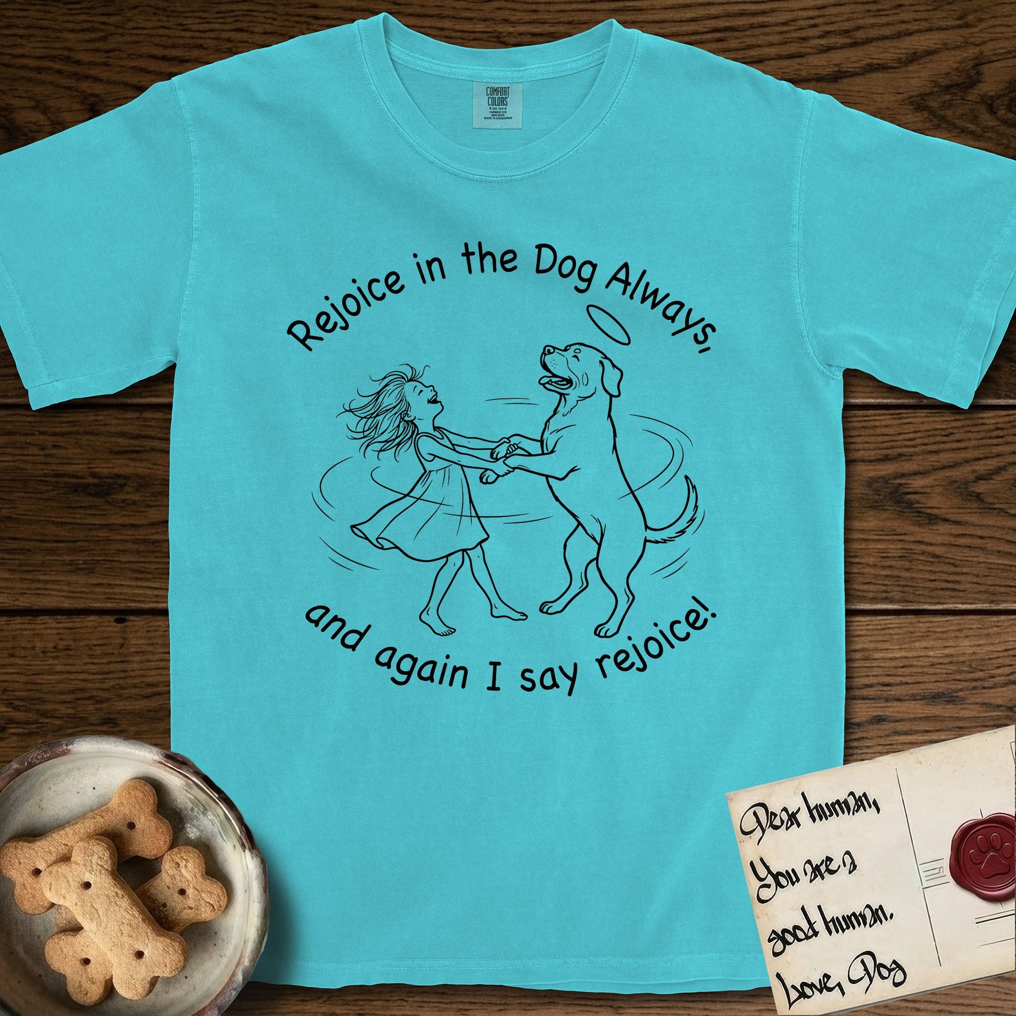 Rejoice in the Dog Rottweiler T-Shirt flat lay in Lagoon Blue, featuring a sparse pen-and-ink illustration of a girl and her Rottweiler dancing on her hind legs, both heads thrown back in joy.