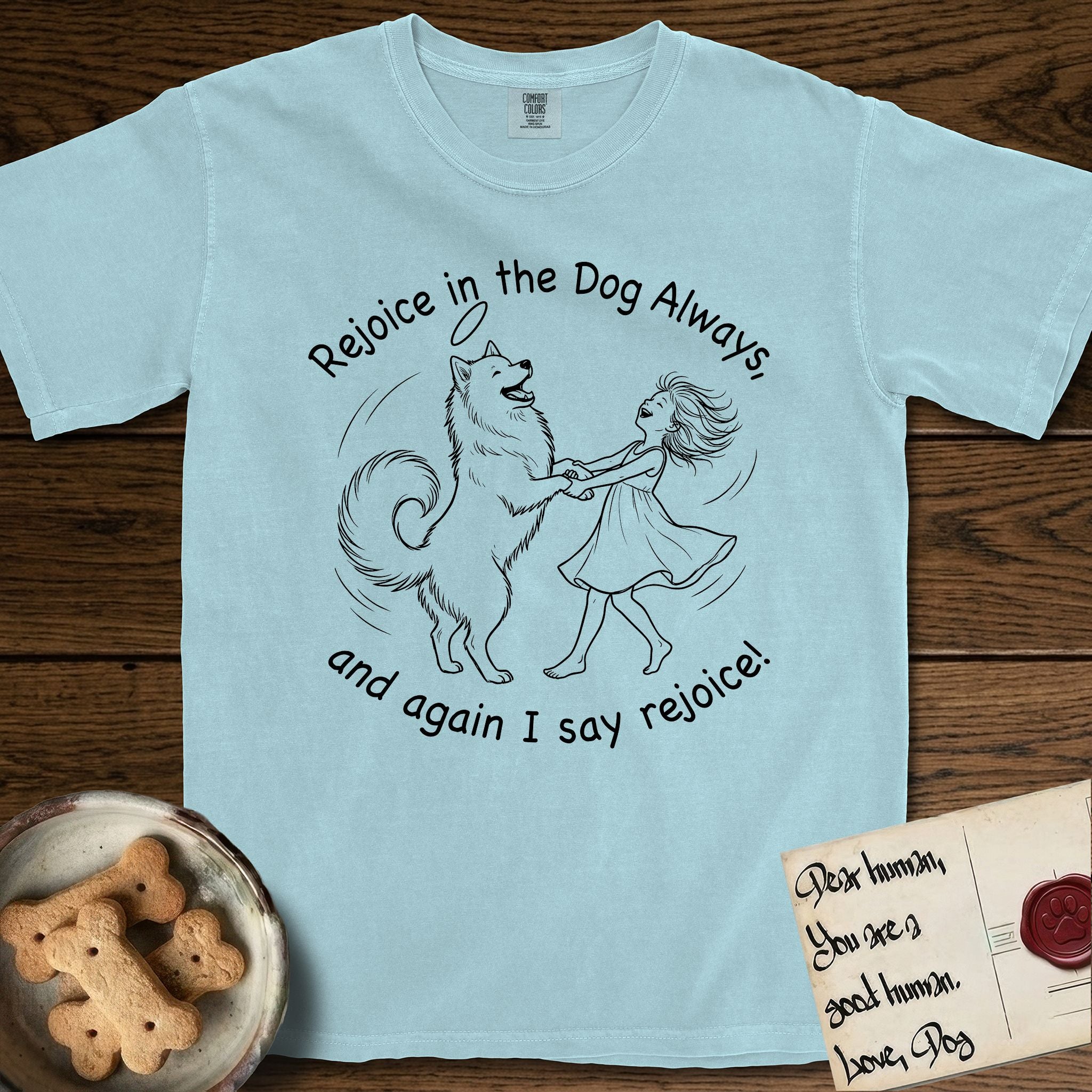 Rejoice in the Dog Samoyed T-Shirt flat lay in Chambray, featuring a sparse pen-and-ink illustration of a girl and her smiling Samoyed spinning together, hands and paws clasped.