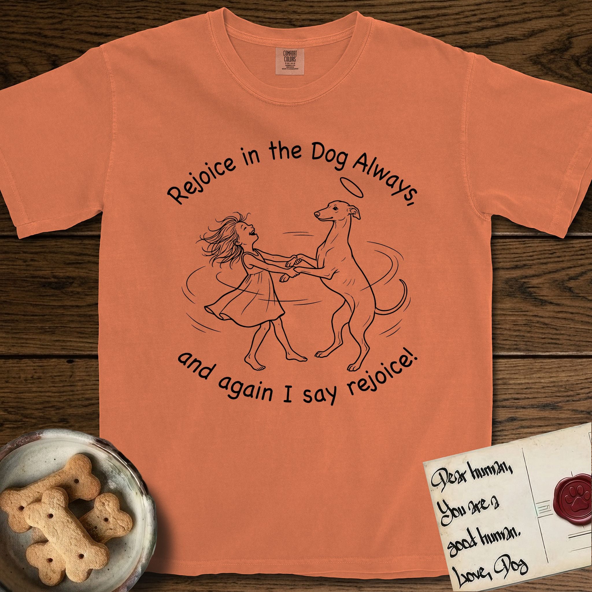 Rejoice in the Dog Whippet T-Shirt flat lay in Melon, featuring a sparse pen-and-ink illustration of a girl and her Whippet dancing on his hind legs, both heads thrown back in joy.