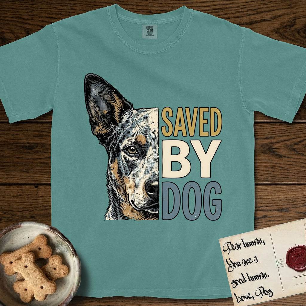 Saved by Dog Australian Cattle Dog T-Shirt flat lay in Blue Spruce, featuring half an Australian Cattle Dog's face in distressed vintage screen print, blue-speckled with tan points and one amber eye, cropped down the centerline beside bold stacked block lettering.