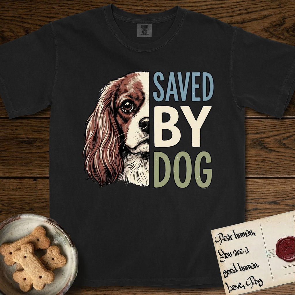 Saved by Dog Cavalier T-Shirt flat lay in Black, featuring half a chestnut-and-white Cavalier's face in distressed vintage screen print, one long feathered ear and a large soft eye, cropped down the centerline beside bold stacked block lettering.