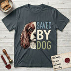 Saved by Dog Cavalier T-Shirt flat lay in Dark Heather Grey, featuring half a chestnut-and-white Cavalier's face in distressed vintage screen print, one long feathered ear and a large soft eye, cropped down the centerline beside bold stacked block lettering.