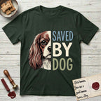 Saved by Dog Cavalier T-Shirt flat lay in Forest Green, featuring half a chestnut-and-white Cavalier's face in distressed vintage screen print, one long feathered ear and a large soft eye, cropped down the centerline beside bold stacked block lettering.