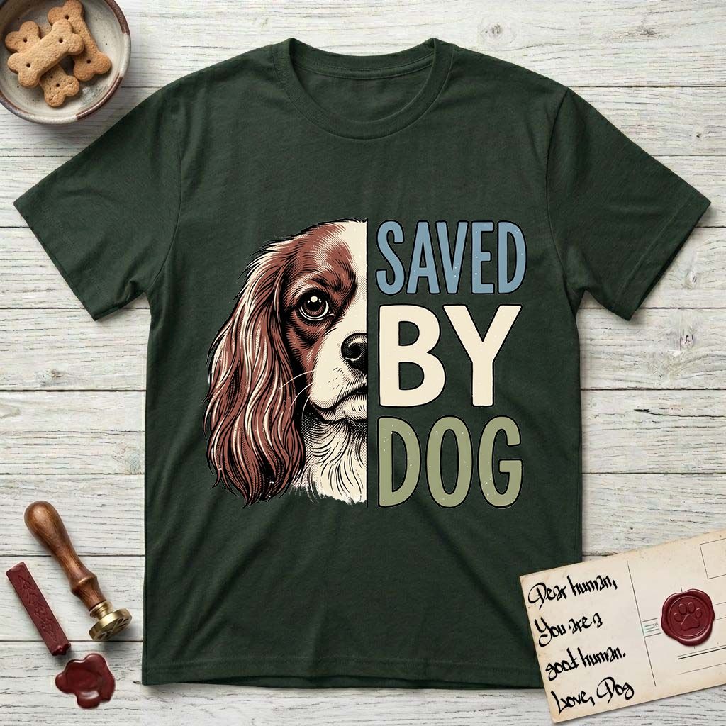 Saved by Dog Cavalier T-Shirt flat lay in Forest Green, featuring half a chestnut-and-white Cavalier's face in distressed vintage screen print, one long feathered ear and a large soft eye, cropped down the centerline beside bold stacked block lettering.
