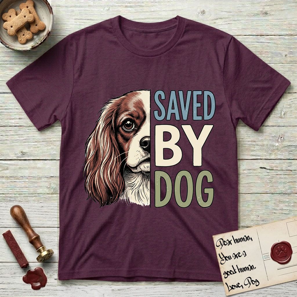 Saved by Dog Cavalier T-Shirt flat lay in Maroon, featuring half a chestnut-and-white Cavalier's face in distressed vintage screen print, one long feathered ear and a large soft eye, cropped down the centerline beside bold stacked block lettering.
