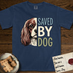 Saved by Dog Cavalier T-Shirt flat lay in True Navy, featuring half a chestnut-and-white Cavalier's face in distressed vintage screen print, one long feathered ear and a large soft eye, cropped down the centerline beside bold stacked block lettering.