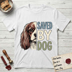 Saved by Dog Cavalier T-Shirt flat lay in White, featuring half a chestnut-and-white Cavalier's face in distressed vintage screen print, one long feathered ear and a large soft eye, cropped down the centerline beside bold stacked block lettering.