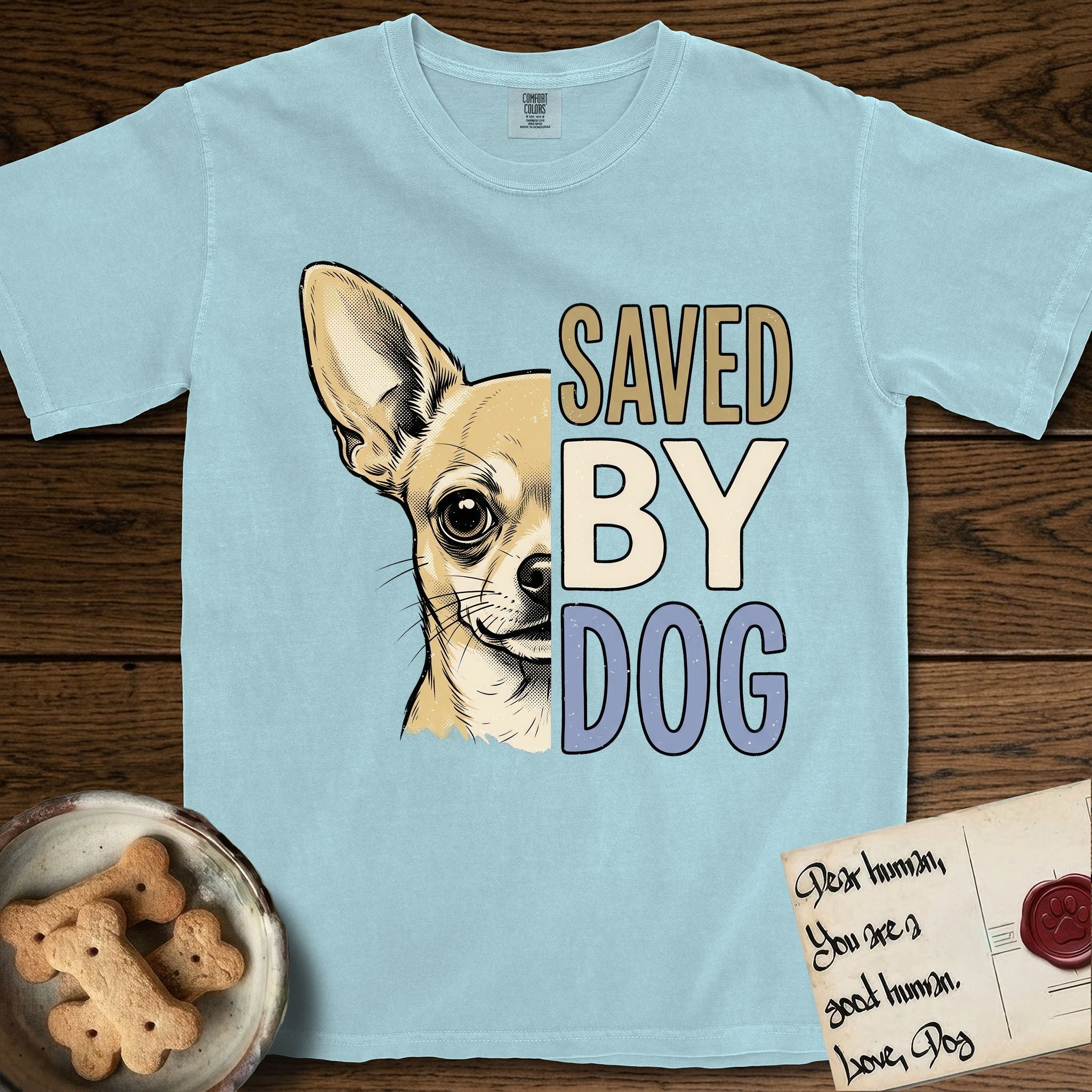 Saved by Dog Chihuahua T-Shirt flat lay in Chambray, featuring half a fawn Chihuahua's face in distressed vintage screen print, one huge upright ear and an enormous dark eye, cropped down the centerline beside bold stacked block lettering.