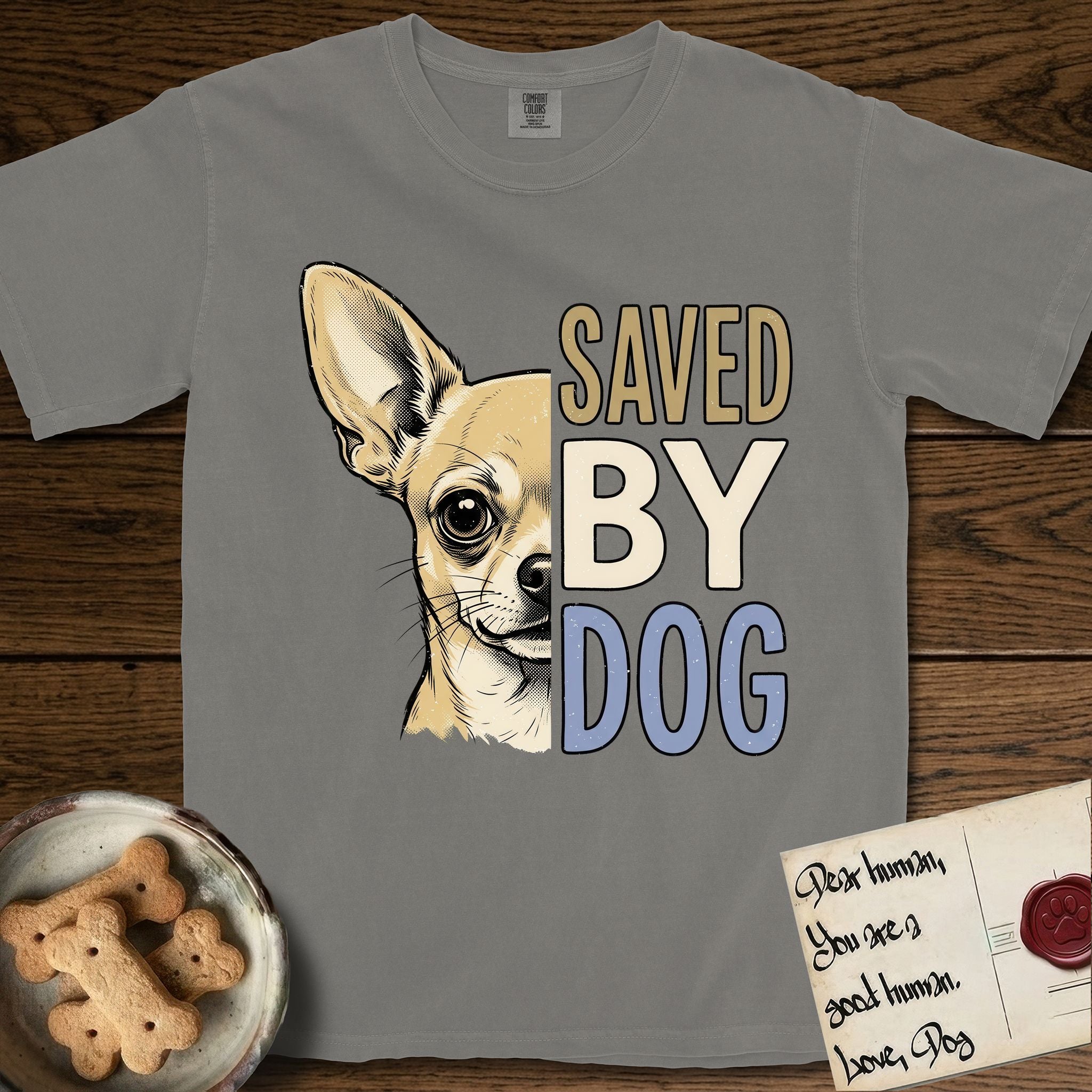 Saved by Dog Chihuahua T-Shirt flat lay in Grey, featuring half a fawn Chihuahua's face in distressed vintage screen print, one huge upright ear and an enormous dark eye, cropped down the centerline beside bold stacked block lettering.