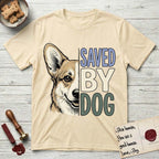 Saved by Dog Corgi T-Shirt flat lay in Natural, featuring half a tan-and-cream Corgi's face in distressed vintage screen print, one upright ear and a foxy grin, cropped down the centerline beside bold stacked block lettering.