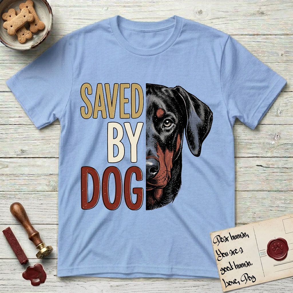 Saved by Dog Doberman T-Shirt flat lay in Light Blue, featuring half a black-and-rust Doberman's face in distressed vintage screen print, natural uncropped ears and a steady eye, cropped down the centerline beside bold stacked block lettering.