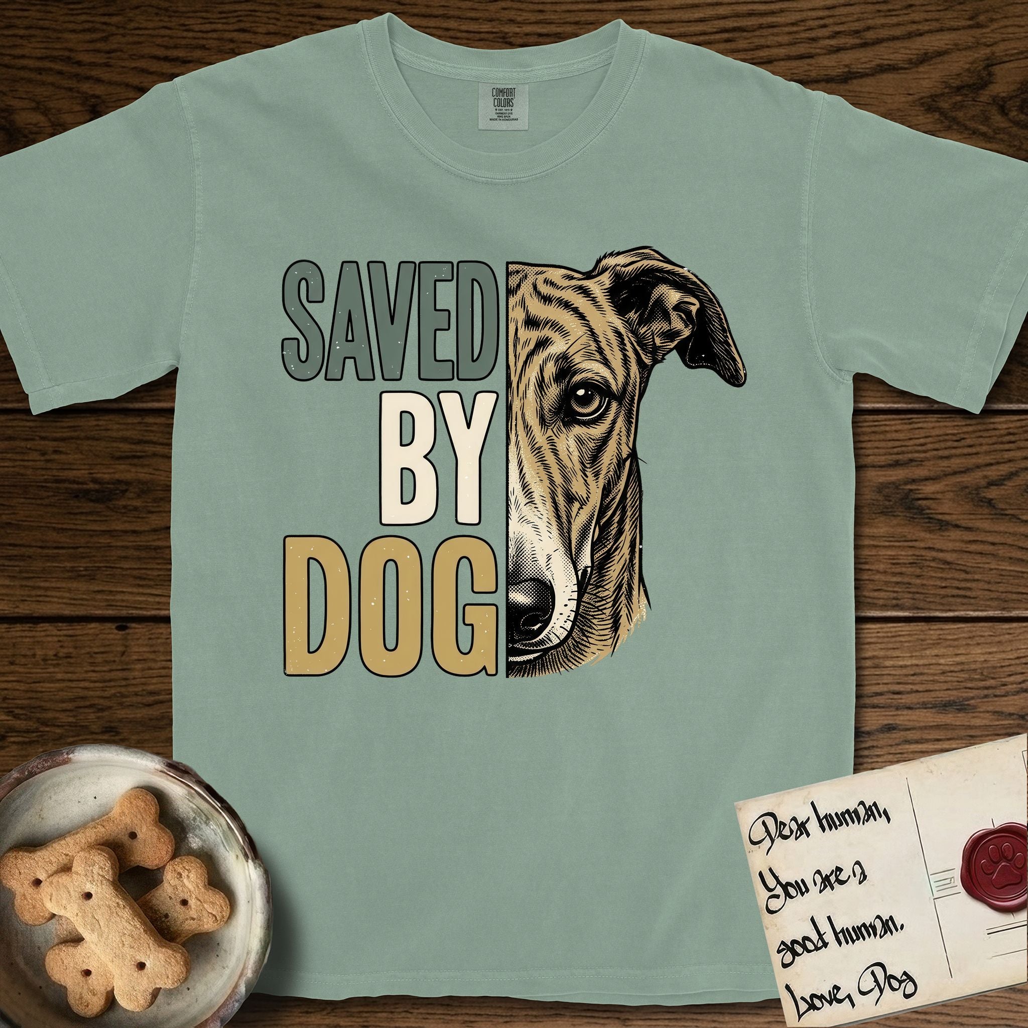 Saved by Dog Galgo T-Shirt flat lay in Bay, featuring half a brindle Galgo's face in distressed vintage screen print, a folded rose ear and a gentle eye, cropped down the centerline beside bold stacked block lettering.
