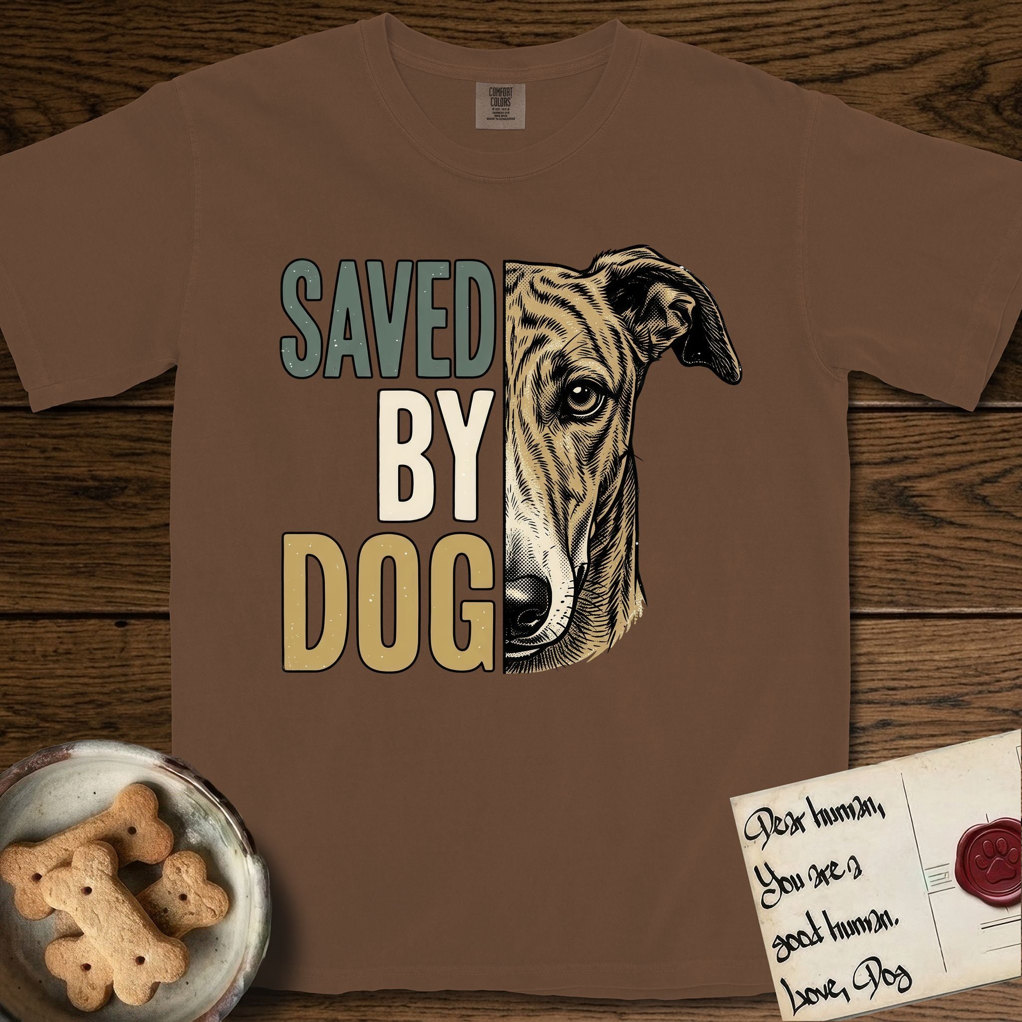 Saved by Dog Galgo T-Shirt flat lay in Espresso, featuring half a brindle Galgo's face in distressed vintage screen print, a folded rose ear and a gentle eye, cropped down the centerline beside bold stacked block lettering.