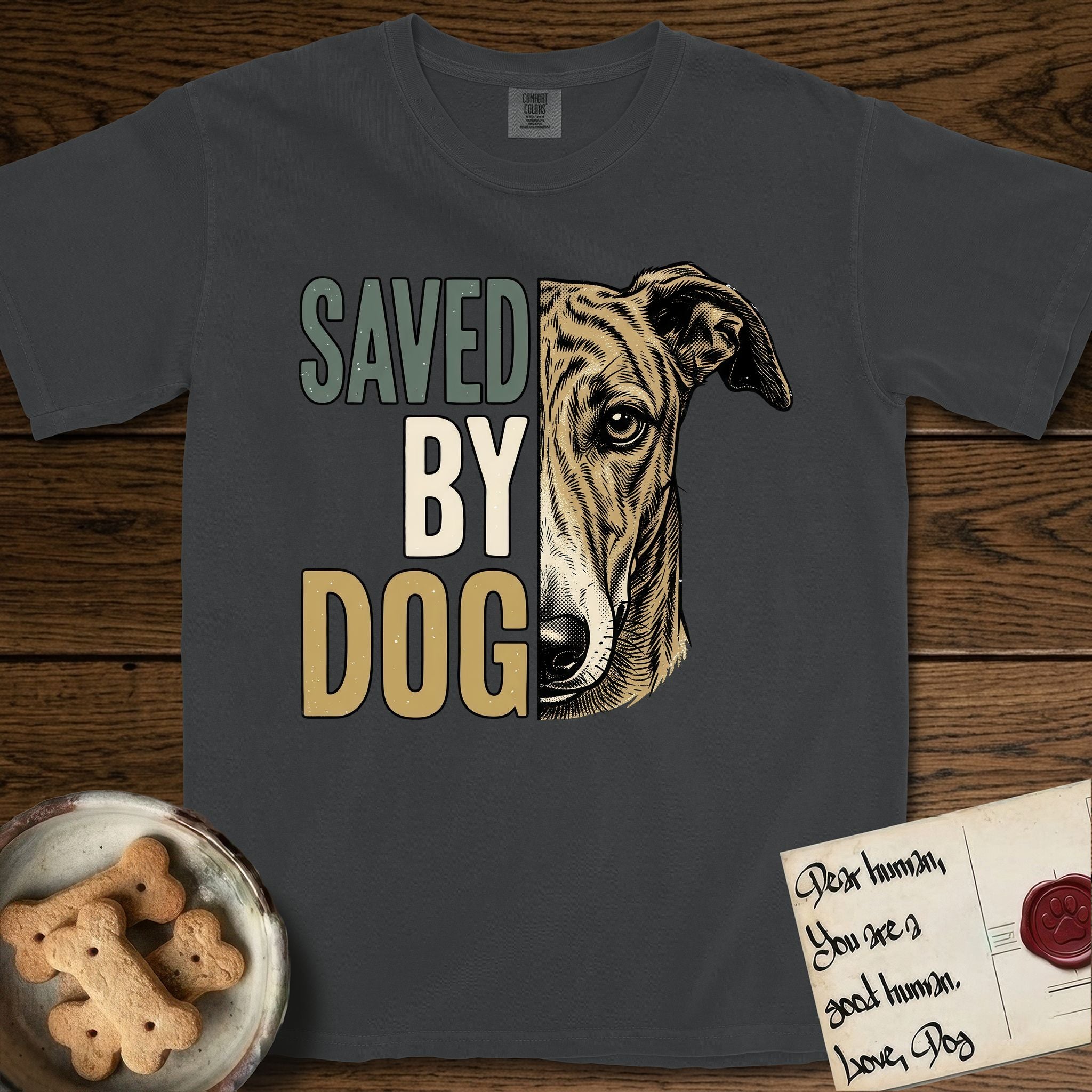 Saved by Dog Galgo T-Shirt flat lay in Graphite, featuring half a brindle Galgo's face in distressed vintage screen print, a folded rose ear and a gentle eye, cropped down the centerline beside bold stacked block lettering.