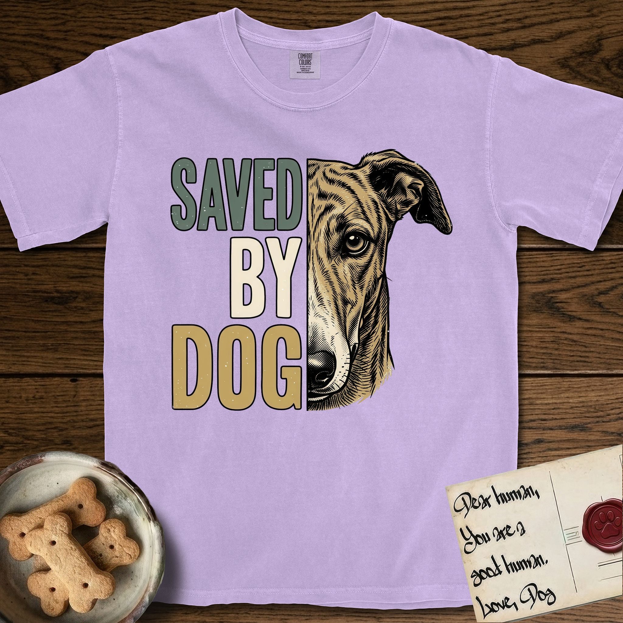 Saved by Dog Galgo T-Shirt flat lay in Orchid, featuring half a brindle Galgo's face in distressed vintage screen print, a folded rose ear and a gentle eye, cropped down the centerline beside bold stacked block lettering.