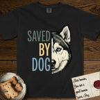 Saved by Dog Husky T-Shirt flat lay in Black, featuring half a black-and-white Husky's face in distressed vintage screen print, one pale ice-blue eye, cropped down the centerline beside bold stacked block lettering.
