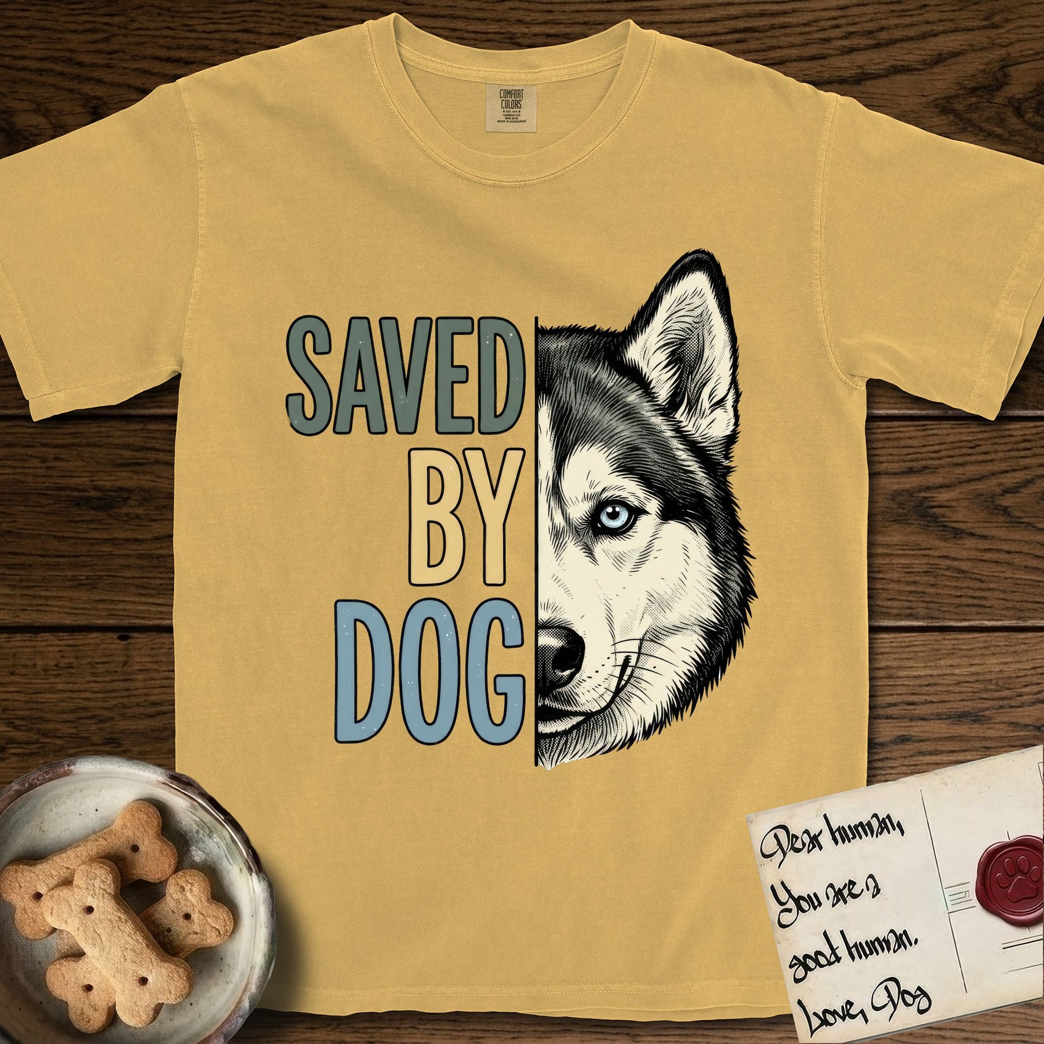 Saved by Dog Husky T-Shirt flat lay in Mustard, featuring half a black-and-white Husky's face in distressed vintage screen print, one pale ice-blue eye, cropped down the centerline beside bold stacked block lettering.