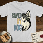 Saved by Dog Husky T-Shirt flat lay in White, featuring half a black-and-white Husky's face in distressed vintage screen print, one pale ice-blue eye, cropped down the centerline beside bold stacked block lettering.