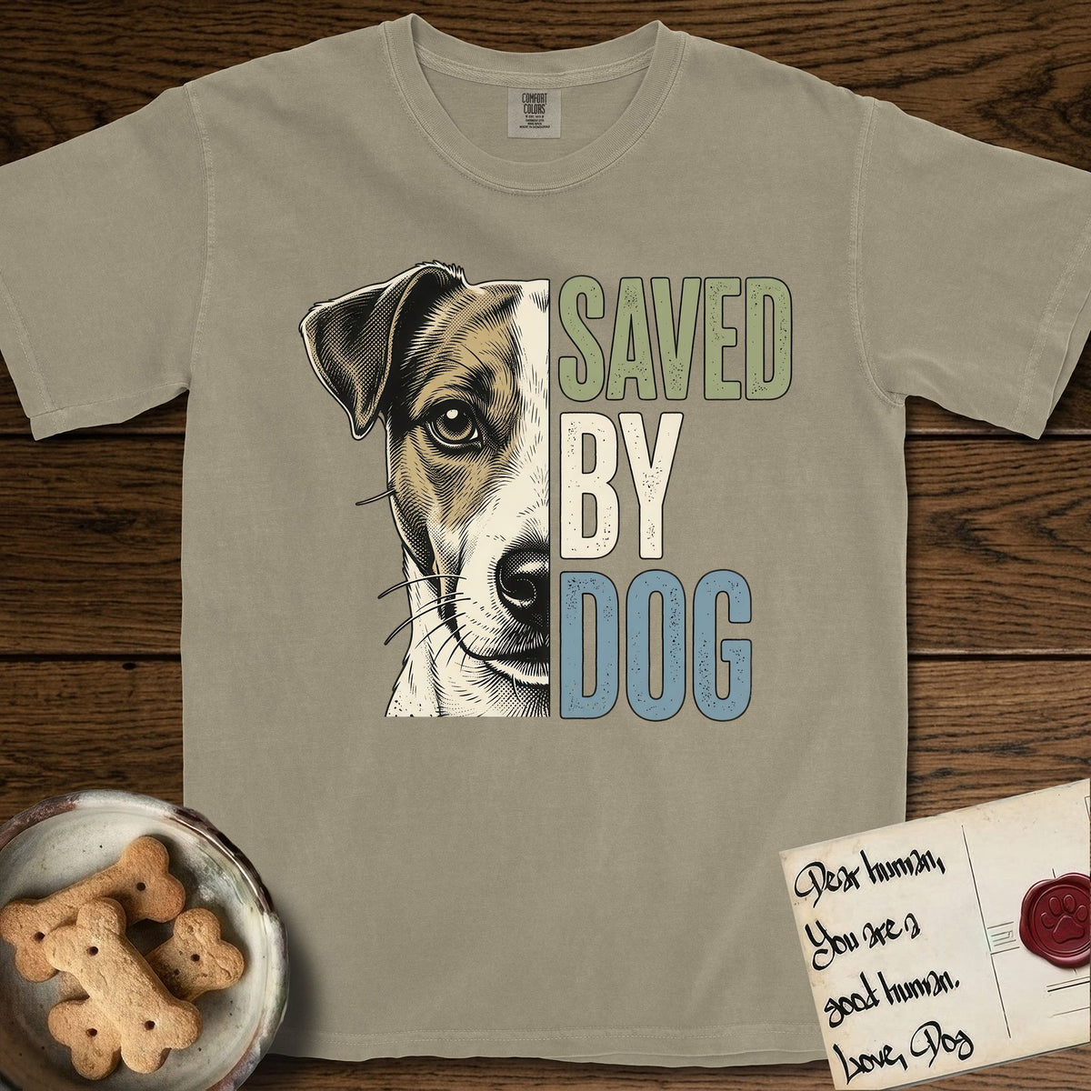 Saved by Dog Jack Russell T-Shirt flat lay in Khaki, featuring half a tan-and-white Jack Russell's face in distressed vintage screen print, a folded ear with a dark patch and forward whiskers, cropped down the centerline beside bold stacked block lettering.