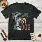 Saved by Dog Pitbull T-Shirt flat lay in Black, featuring half a blue-grey Pitbull's face in distressed vintage screen print, one warm amber eye, cropped down the centerline beside bold stacked block lettering.