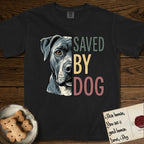 Saved by Dog Pitbull T-Shirt flat lay in Black, featuring half a blue-grey Pitbull's face in distressed vintage screen print, one warm amber eye, cropped down the centerline beside bold stacked block lettering.