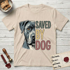 Saved by Dog Pitbull T-Shirt flat lay in Sand, featuring half a blue-grey Pitbull's face in distressed vintage screen print, one warm amber eye, cropped down the centerline beside bold stacked block lettering.