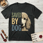 Saved by Dog Poodle T-Shirt flat lay in Black, featuring half an apricot Poodle's face in distressed vintage screen print, soft natural curls and a knowing eye, cropped down the centerline beside bold stacked block lettering.