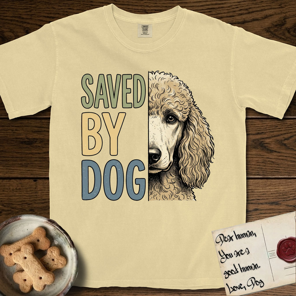 Saved by Dog Poodle T-Shirt flat lay in Butter, featuring half an apricot Poodle's face in distressed vintage screen print, soft natural curls and a knowing eye, cropped down the centerline beside bold stacked block lettering.
