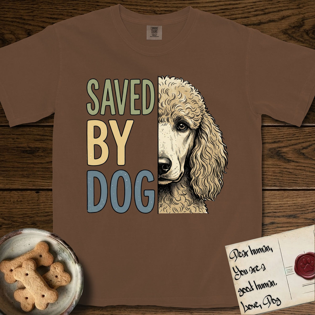 Saved by Dog Poodle T-Shirt flat lay in Espresso, featuring half an apricot Poodle's face in distressed vintage screen print, soft natural curls and a knowing eye, cropped down the centerline beside bold stacked block lettering.