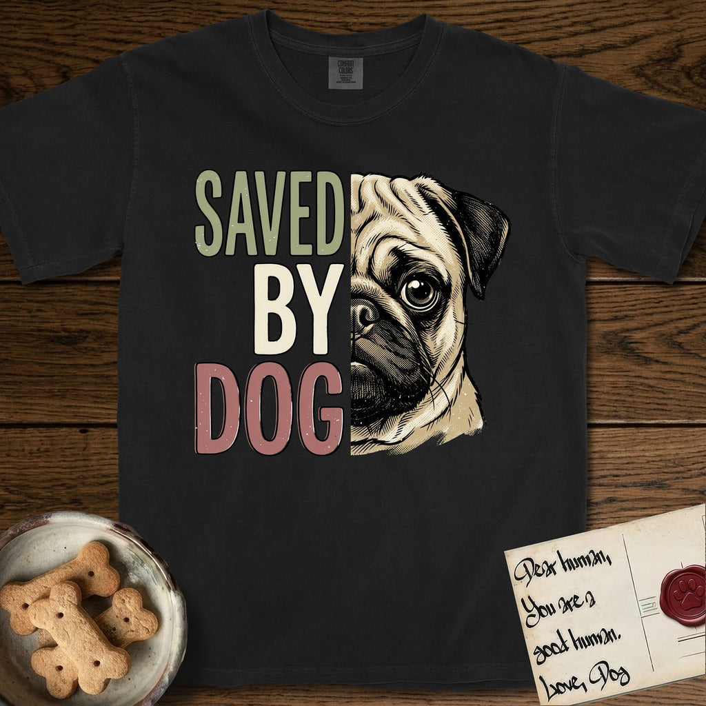 Saved by Dog Pug T-Shirt flat lay in Black, featuring half a fawn Pug's face in distressed vintage screen print, a dark mask and one large round eye, cropped down the centerline beside bold stacked block lettering.