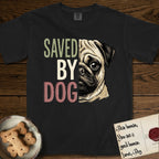 Saved by Dog Pug T-Shirt flat lay in Black, featuring half a fawn Pug's face in distressed vintage screen print, a dark mask and one large round eye, cropped down the centerline beside bold stacked block lettering.