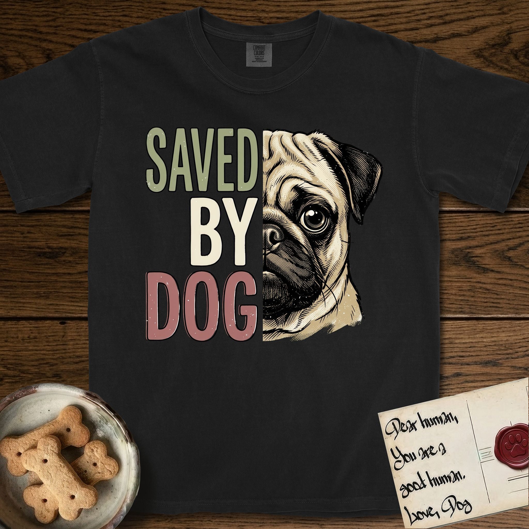 Saved by Dog Pug T-Shirt flat lay in Black, featuring half a fawn Pug's face in distressed vintage screen print, a dark mask and one large round eye, cropped down the centerline beside bold stacked block lettering.
