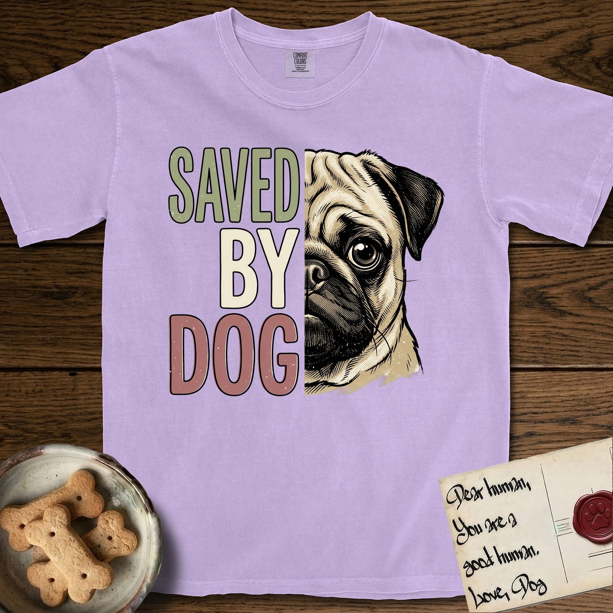Saved by Dog Pug T-Shirt flat lay in Orchid, featuring half a fawn Pug's face in distressed vintage screen print, a dark mask and one large round eye, cropped down the centerline beside bold stacked block lettering.