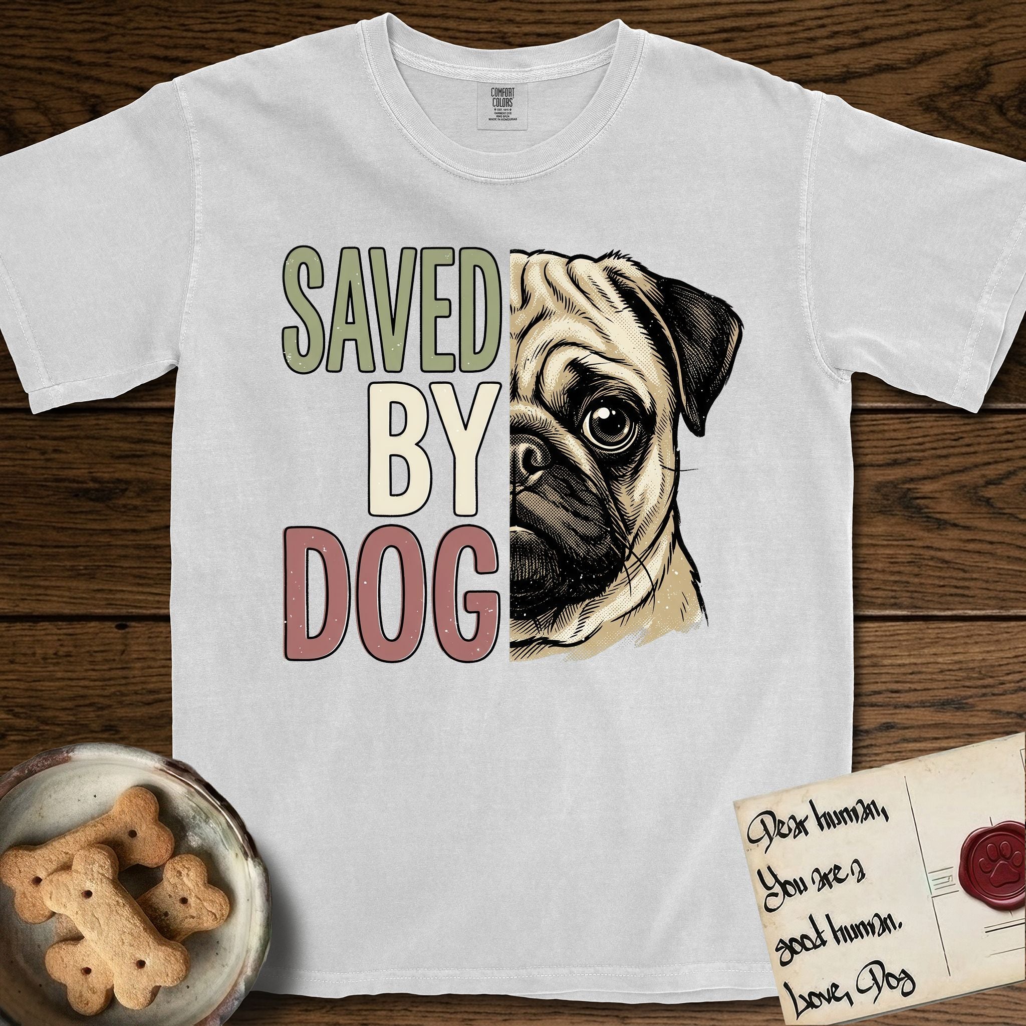 Saved by Dog Pug T-Shirt flat lay in White, featuring half a fawn Pug's face in distressed vintage screen print, a dark mask and one large round eye, cropped down the centerline beside bold stacked block lettering.