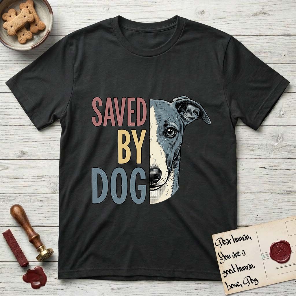 Saved by Dog Whippet T-Shirt flat lay in Black, featuring half a blue-grey Whippet's face in distressed vintage screen print, a folded rose ear and a large liquid eye, cropped down the centerline beside bold stacked block lettering.