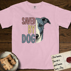 Saved by Dog Whippet T-Shirt flat lay in Blossom, featuring half a blue-grey Whippet's face in distressed vintage screen print, a folded rose ear and a large liquid eye, cropped down the centerline beside bold stacked block lettering.