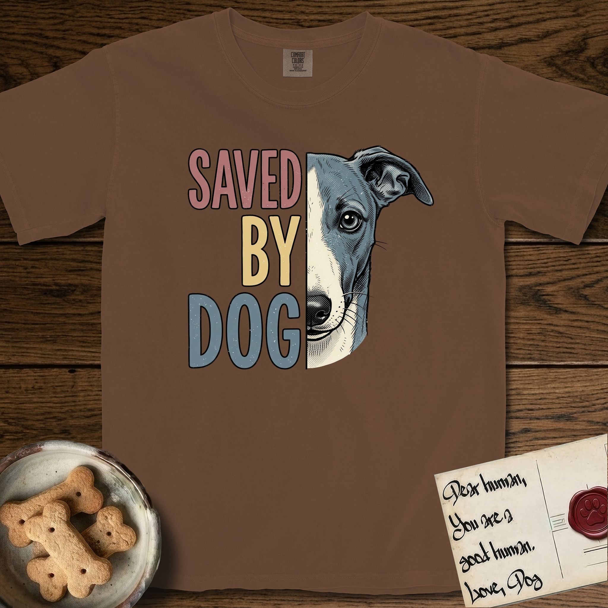 Saved by Dog Whippet T-Shirt flat lay in Espresso, featuring half a blue-grey Whippet's face in distressed vintage screen print, a folded rose ear and a large liquid eye, cropped down the centerline beside bold stacked block lettering.