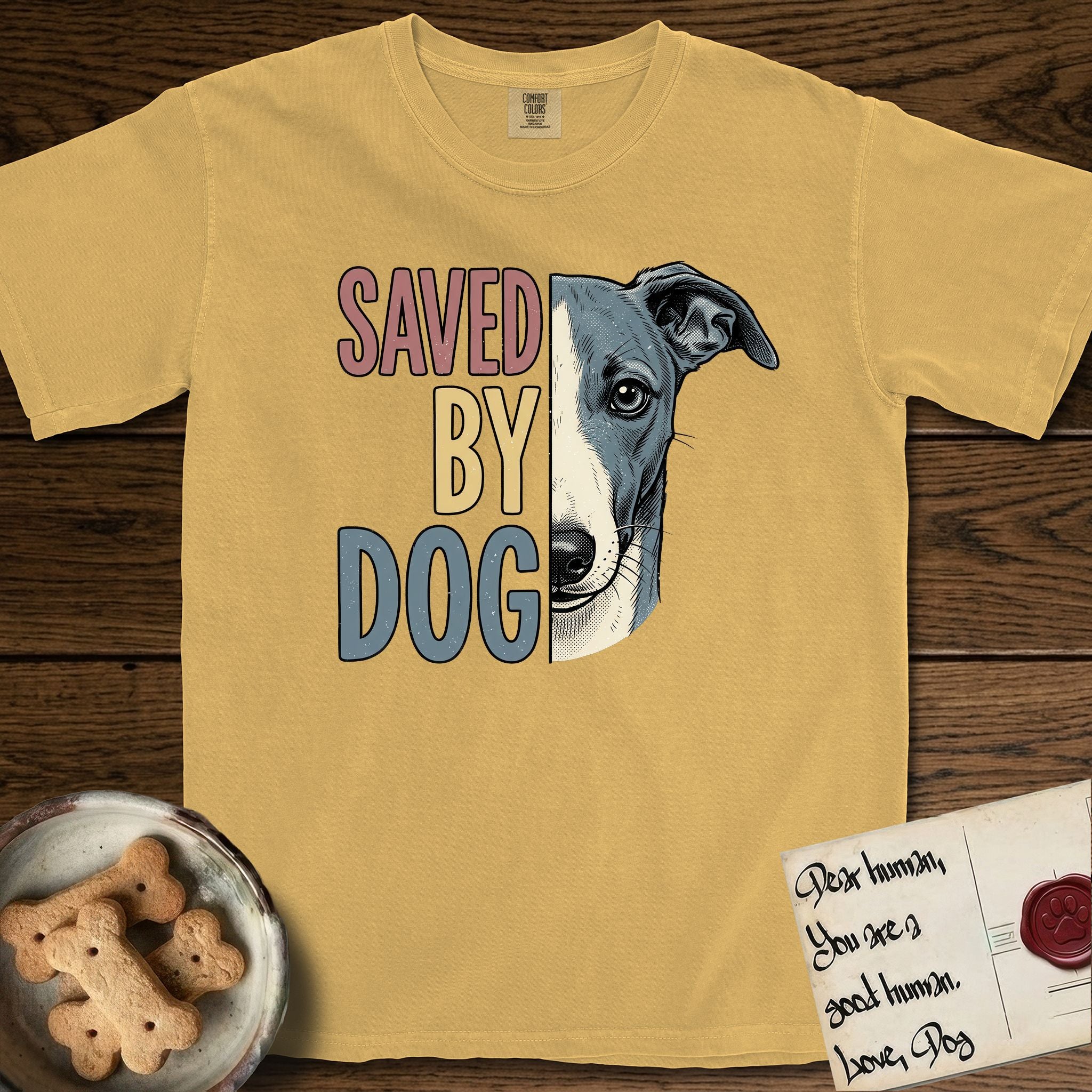 Saved by Dog Whippet T-Shirt flat lay in Mustard, featuring half a blue-grey Whippet's face in distressed vintage screen print, a folded rose ear and a large liquid eye, cropped down the centerline beside bold stacked block lettering.
