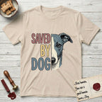 Saved by Dog Whippet T-Shirt flat lay in Sand, featuring half a blue-grey Whippet's face in distressed vintage screen print, a folded rose ear and a large liquid eye, cropped down the centerline beside bold stacked block lettering.