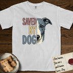 Saved by Dog Whippet T-Shirt flat lay in White, featuring half a blue-grey Whippet's face in distressed vintage screen print, a folded rose ear and a large liquid eye, cropped down the centerline beside bold stacked block lettering.