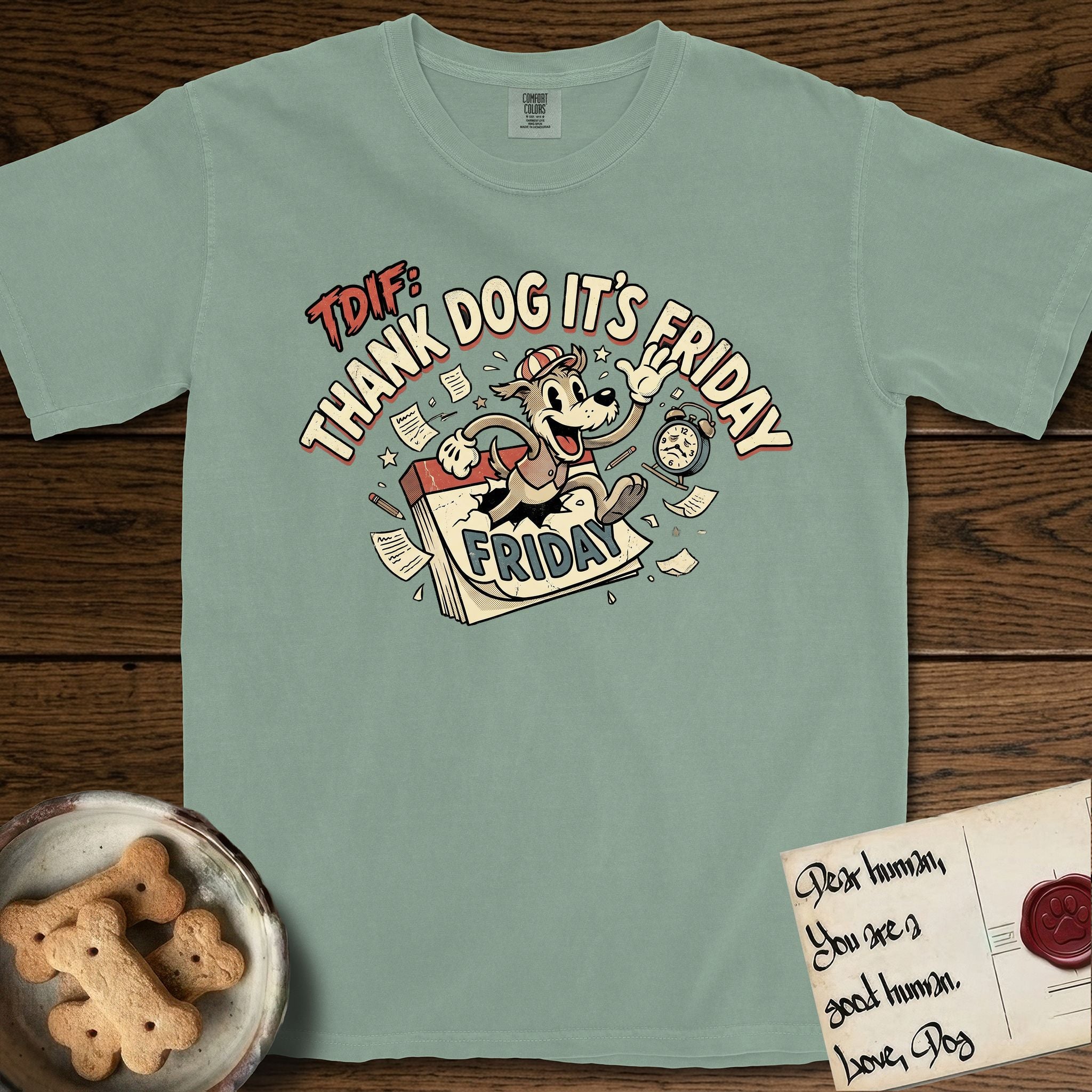 Thank Dog It's Friday T-Shirt flat lay in Bay, featuring a retro 1930s cartoon of a Dog bursting through a Friday calendar page, surrounded by musical notes, stars, and a clock, with retro display lettering reading TDIF.