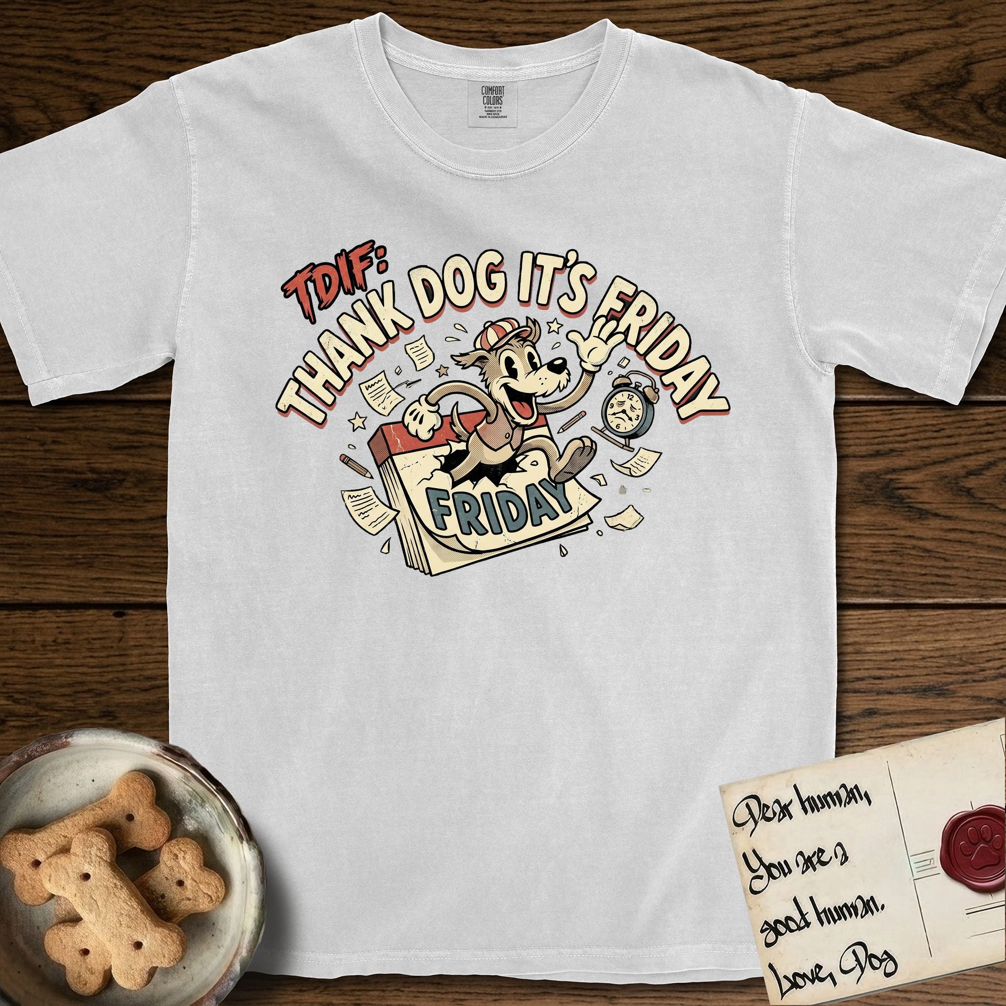 Thank Dog It's Friday T-Shirt flat lay in White, featuring a retro 1930s cartoon of a Dog bursting through a Friday calendar page, surrounded by musical notes, stars, and a clock, with retro display lettering reading TDIF.