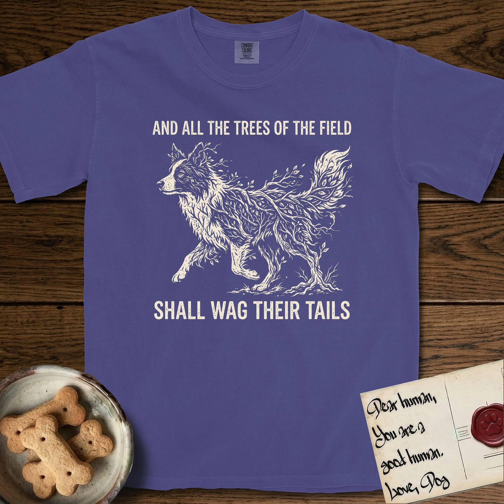 Trees of the Field Border Collie T-Shirt flat lay in Grape, featuring a vintage woodcut illustration of a Border Collie formed of quaking aspen branches, mid-stride, with the words And All the Trees of the Field Shall Wag Their Tails.