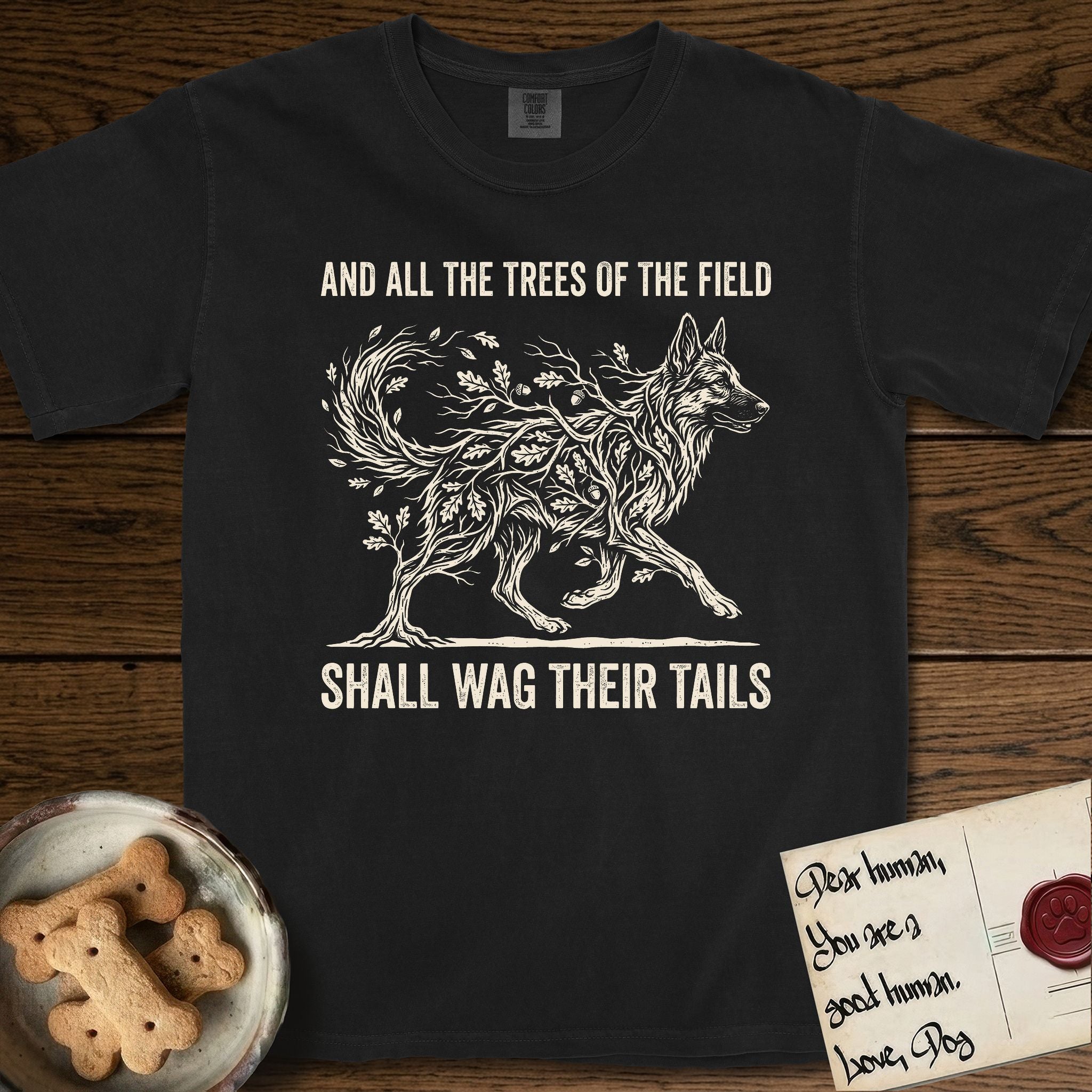 Trees of the Field German Shepherd T-Shirt flat lay in Black, featuring a vintage woodcut illustration of a German Shepherd formed of oak branches with acorns, mid-stride, with the words And All the Trees of the Field Shall Wag Their Tails.